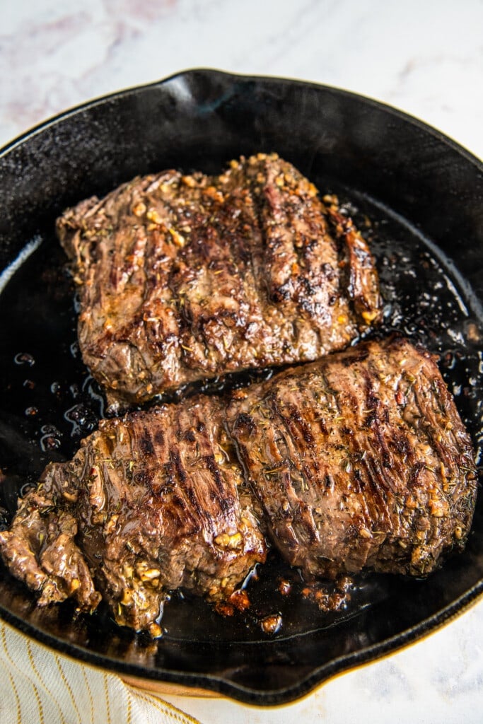 Two skirt steaks cooking in a cast iron skillet