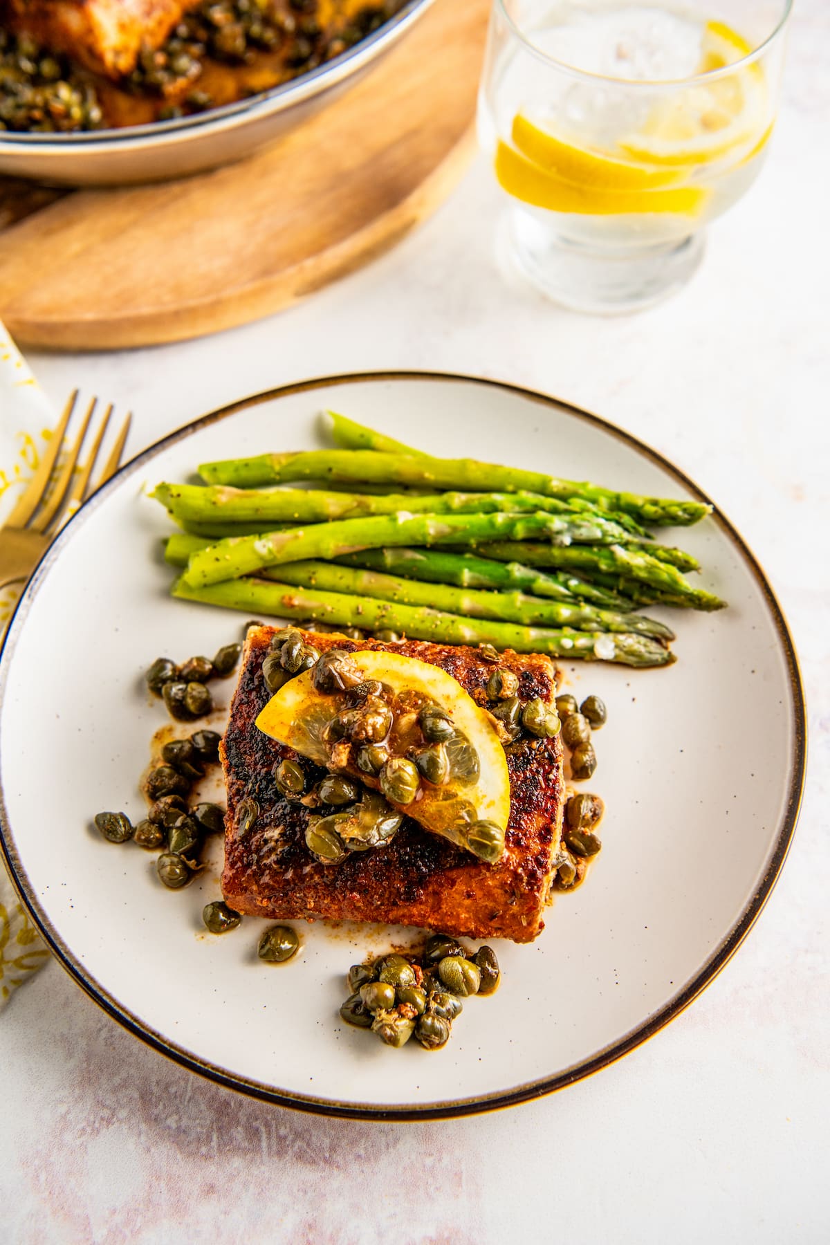 Overhead view of a plate of seared mahi mahi topped with lemon and capers, next to asparagus