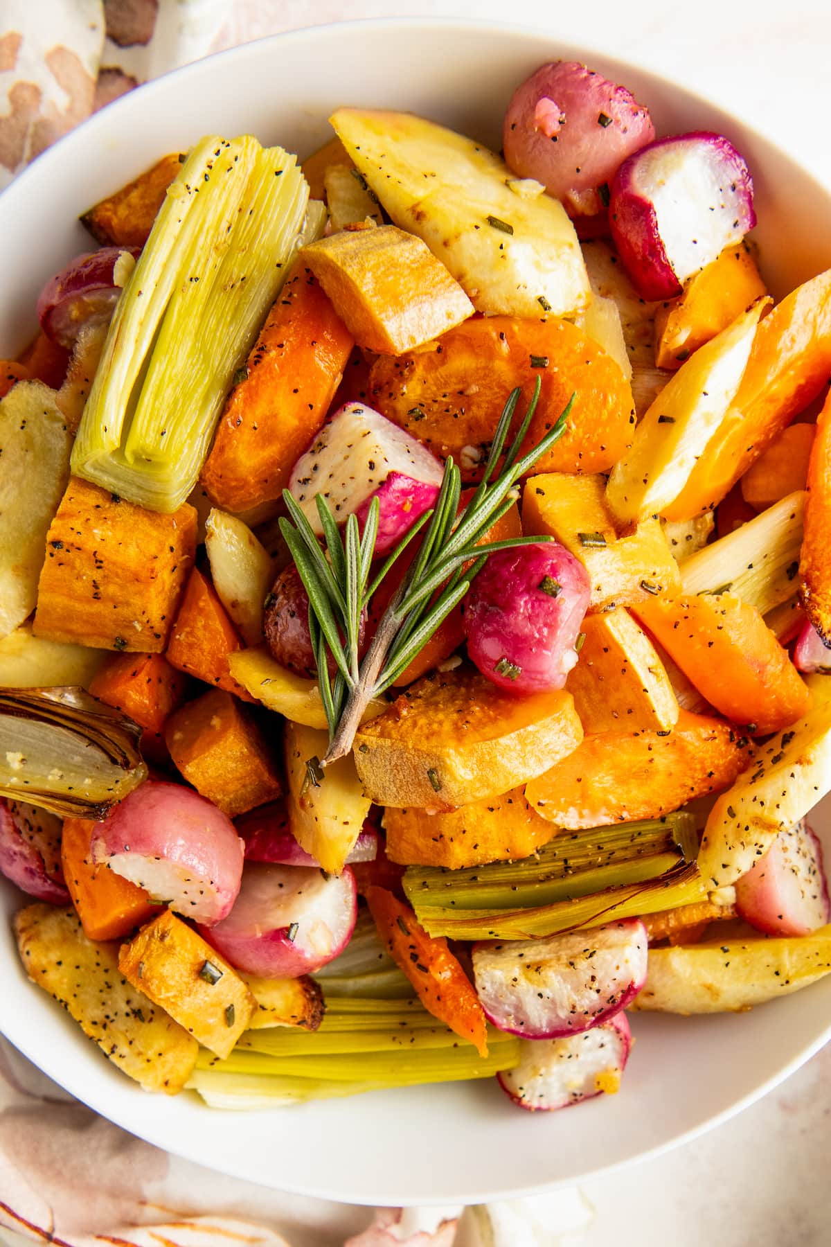 Overhead view of a plate full of roasted root vegetables, topped with a sprig of parsley