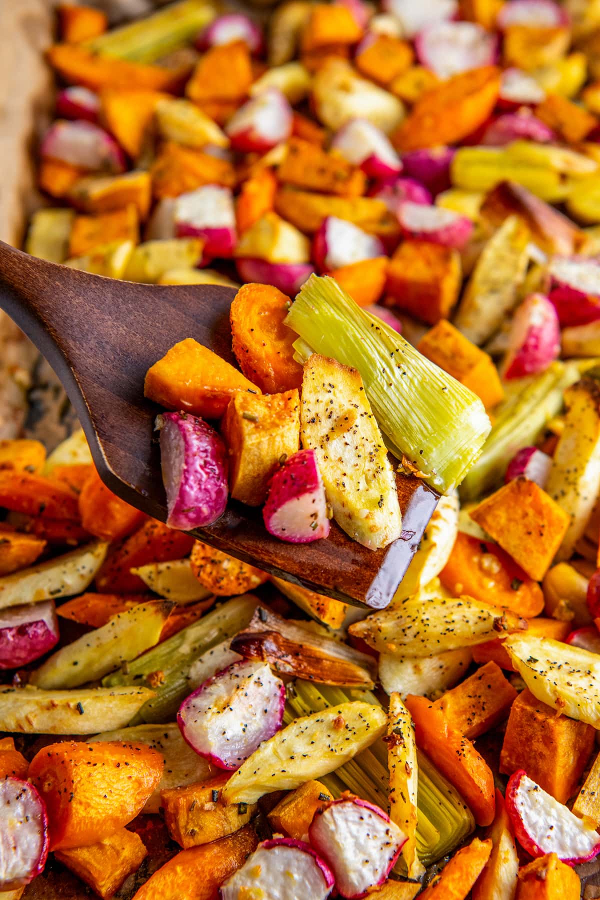 A tray of roasted root vegetables, with a wooden spatula picking some out