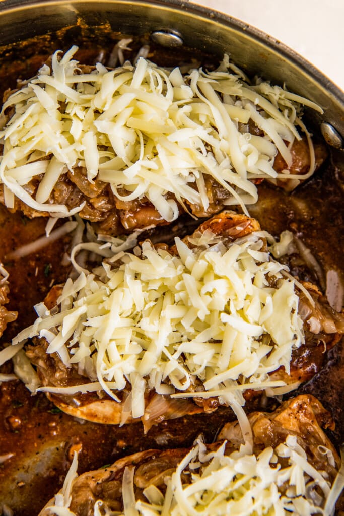Overhead view of three chicken breasts topped with caramelized onions and unmelted, shredded gruyere cheese
