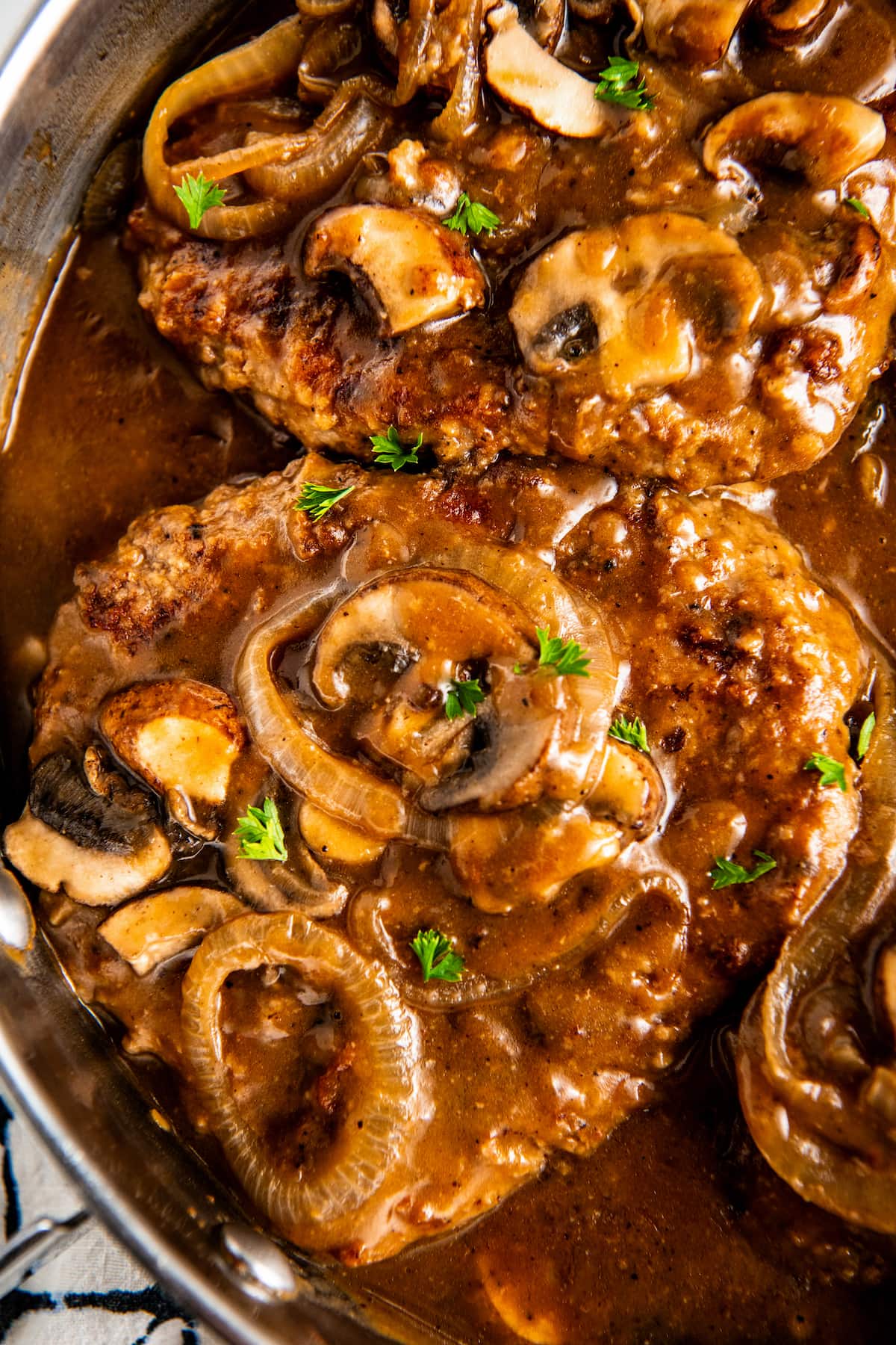 Overhead view of two steaks covered in mushrooms, cooking in gravy