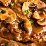 Close up of steak covered in gravy and mushrooms