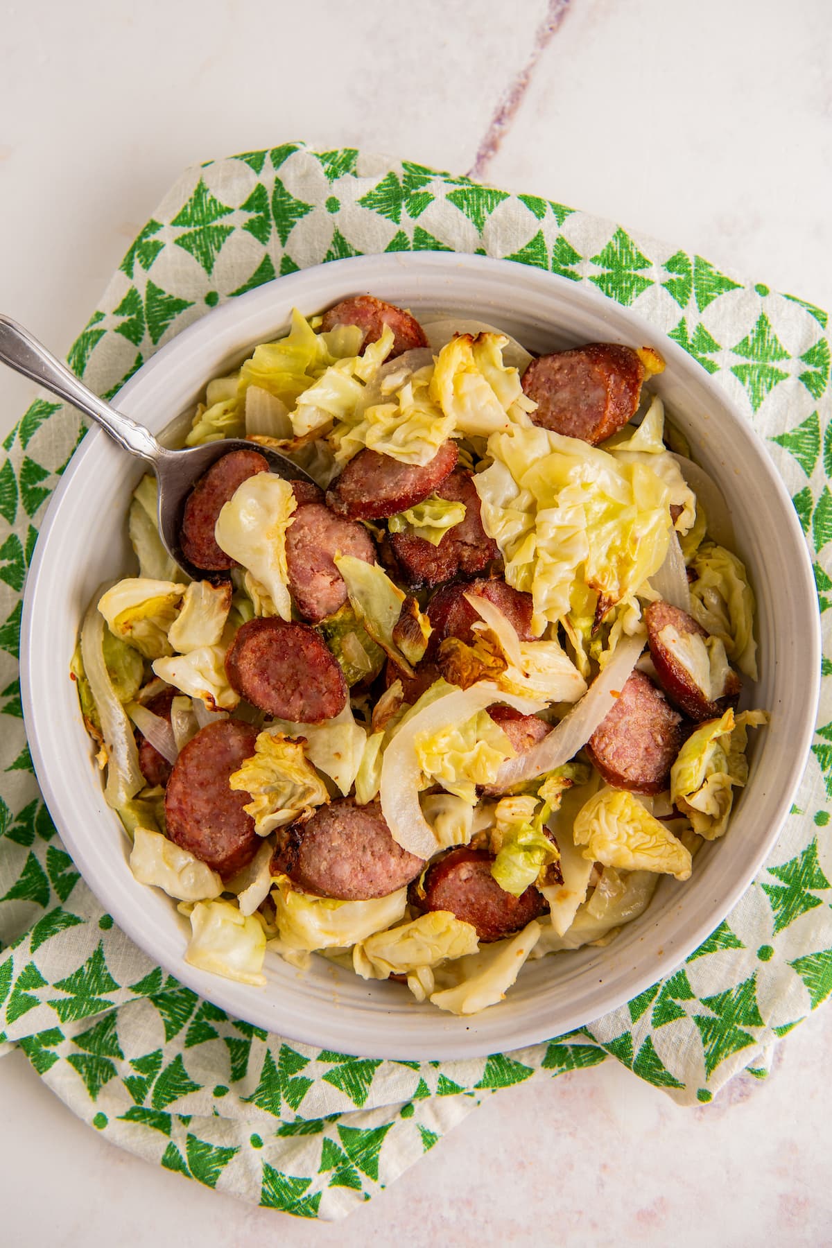 A bowl filled with air fried cabbage and sausage with a spoon scooping out a serving.