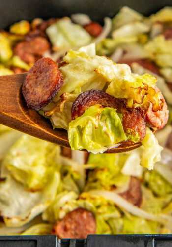Close up of sausage and cabbage on a wooden spoon, above a serving dish of it