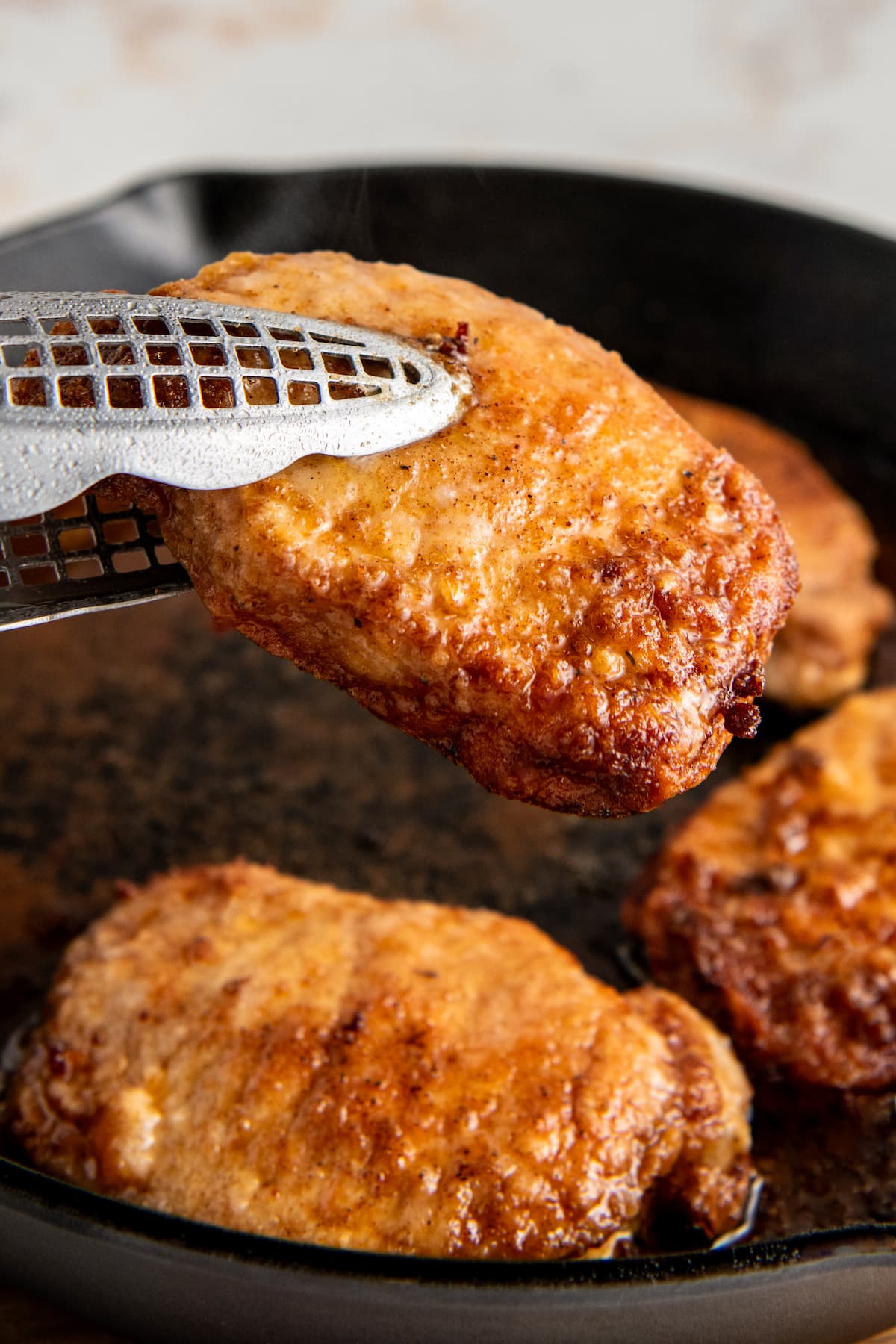 Tongs removing a crispy pork chop from a skillet
