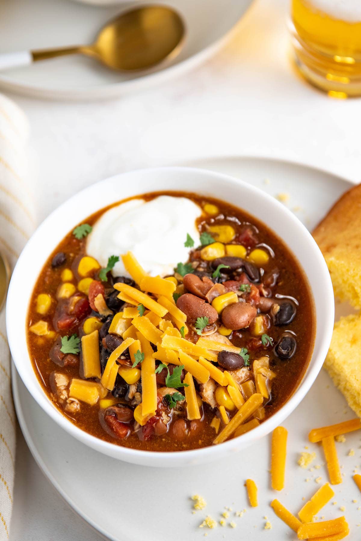 A bowl of chicken chili topped with shredded cheese and sour cream.