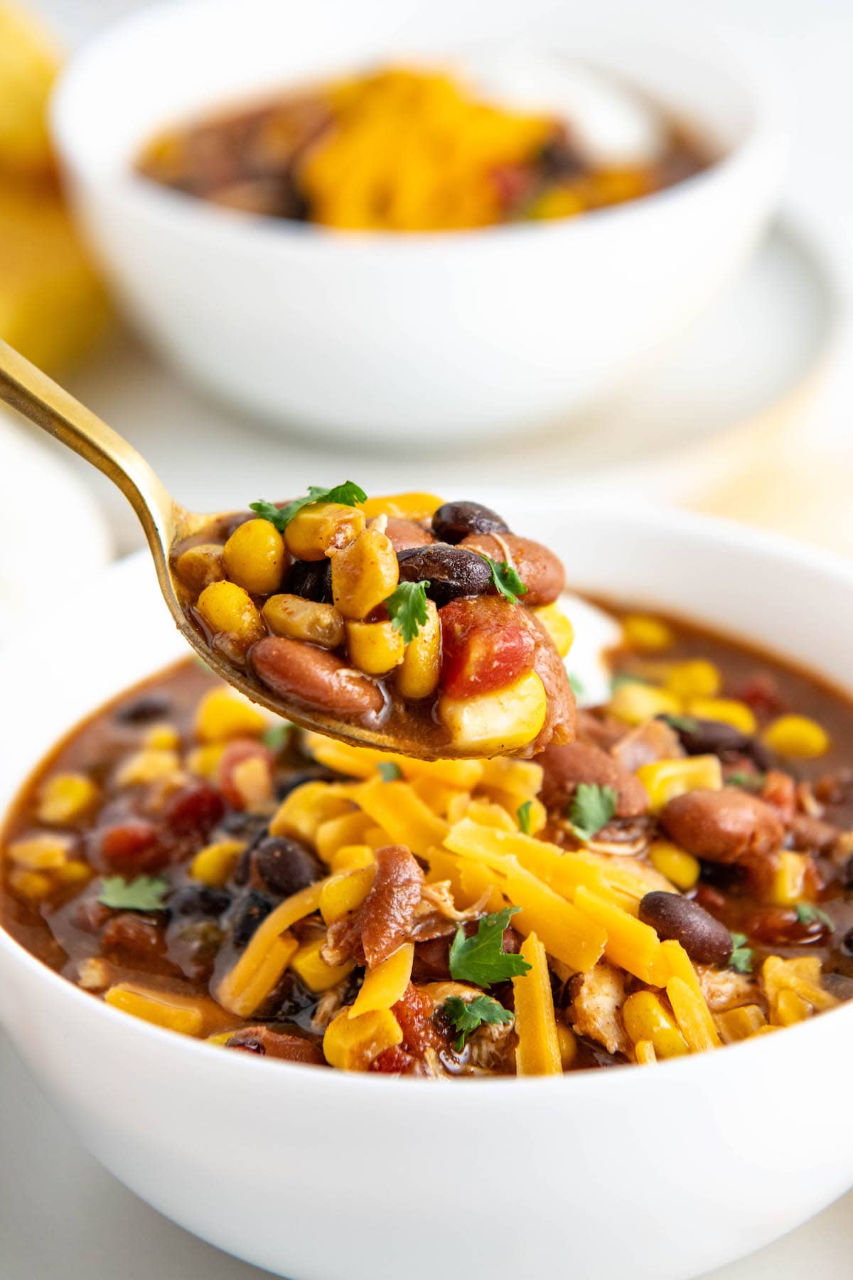 A spoonful of chili hovering over a bowl of chili topped with cheese.