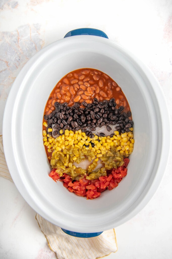Overhead view of a crockpot with a row of chili beans, a row of black beans, a row of corn, a row of green chilis, and a row of rotel.