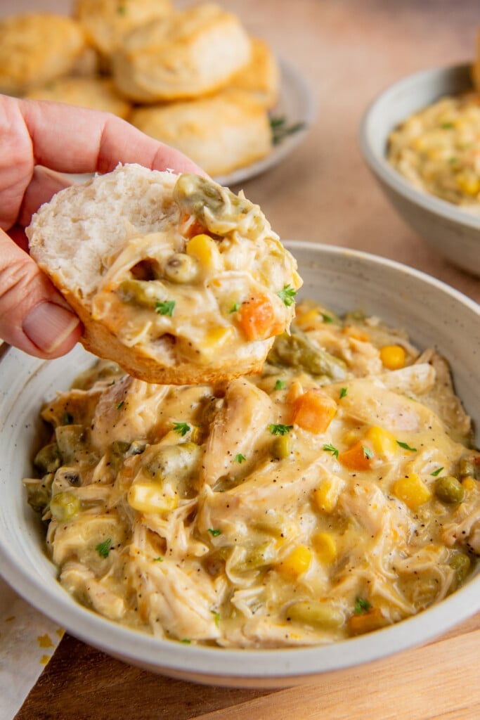 A biscuit is being dipped into slow cooker chicken pot pie. 