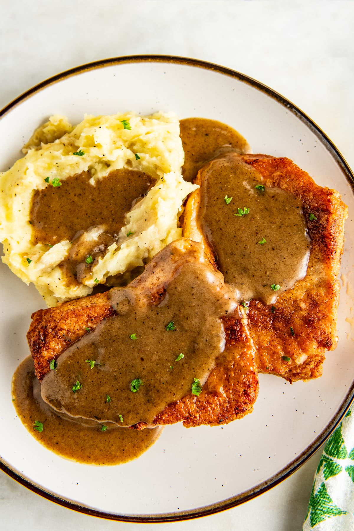 Overhead view of a plate with two pork chops and a pile of mashed potatoes, all covered in gravy.