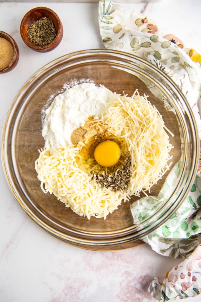 Overhead view of a bowl with an egg, ricotta cheese, parmesan cheese, mozzarella cheese, and spices