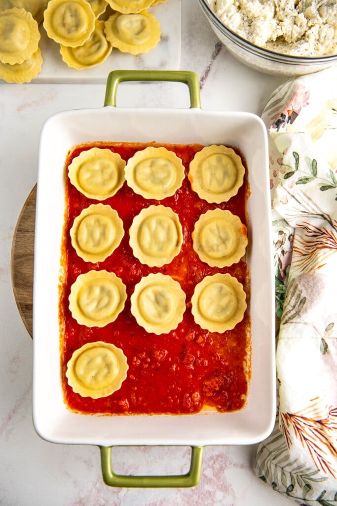 Overhead view of uncooked ravioli in a casserole dish on top of marinara sauce