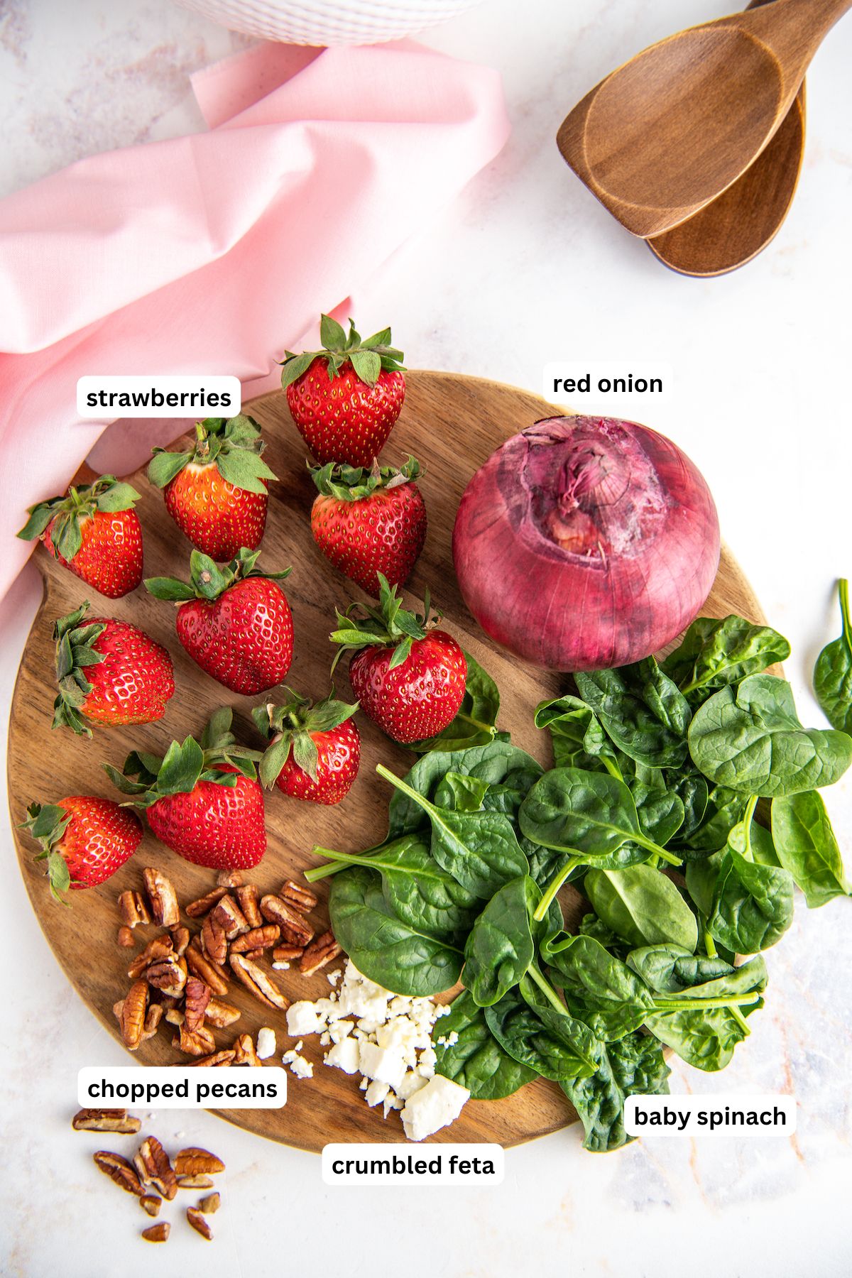 Spinach and strawberry salad ingredients in order from top to bottom: strawberries, red onion, baby spinach, crumbled feta, chopped pecans.