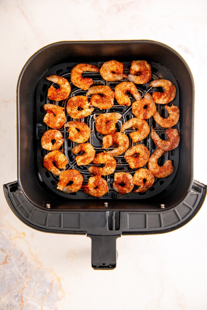 Seasoned shrimp in a single layer in an air fryer basket.