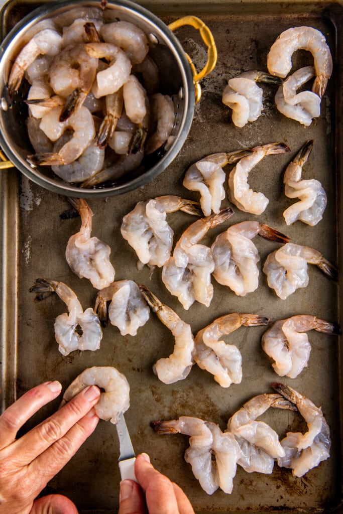 Spreading butterflied shrimp out on a baking sheet.