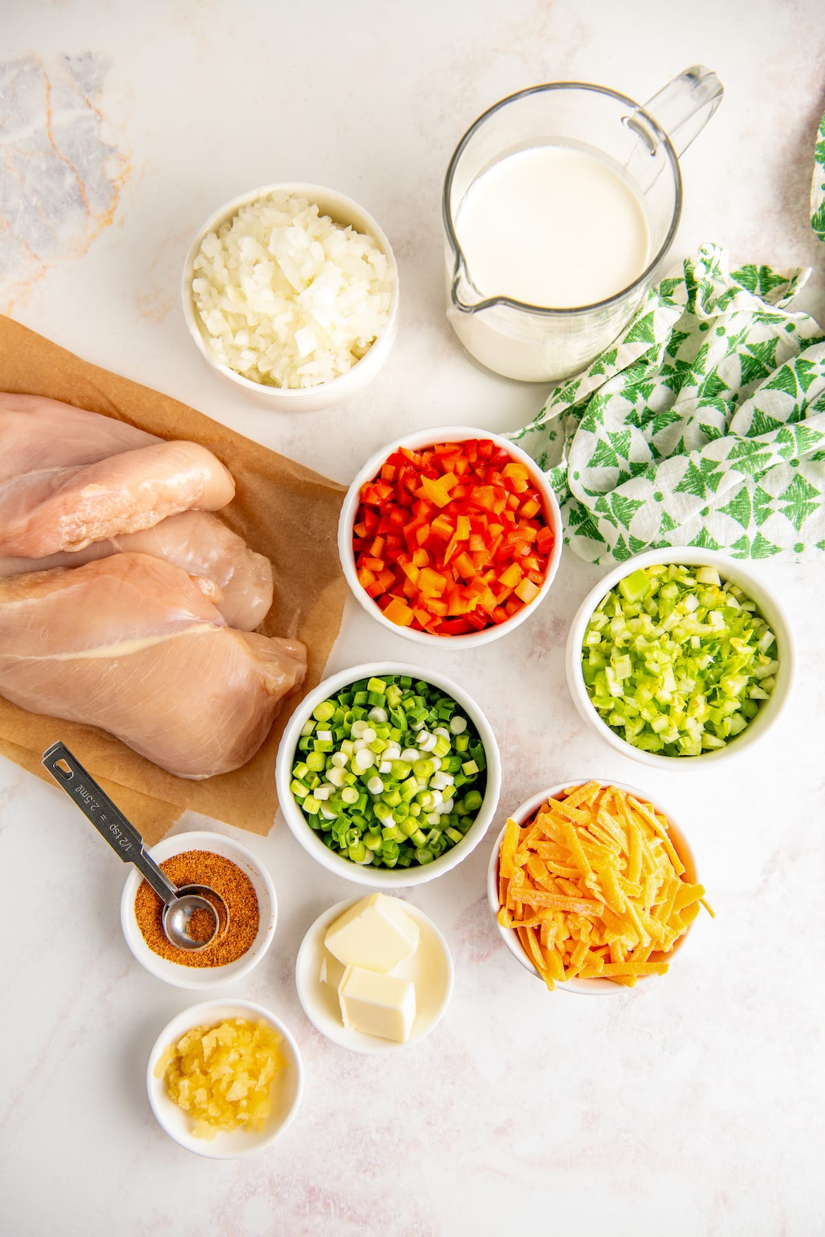 Ingredients in bowls arranged on a work surface with chicken breasts on parchment paper. 