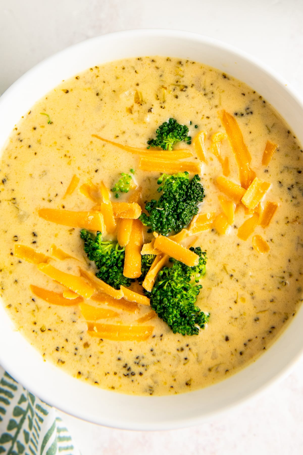 Overhead shot of crockpot broccoli cheese soup garnished with broccoli and shredded cheddar.