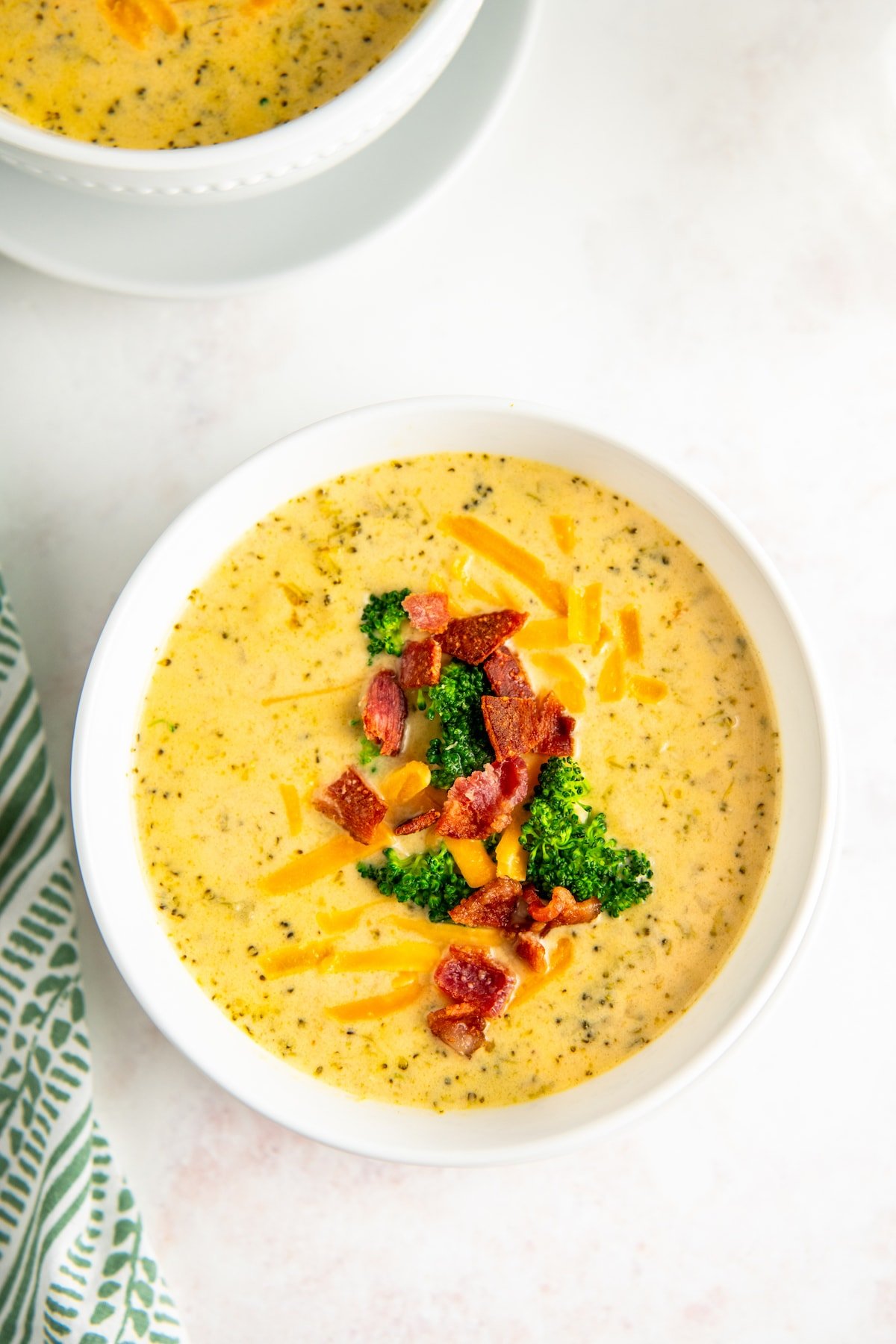 A bowl of soup, garnished with shredded cheese, bacon bits, and broccoli florets.