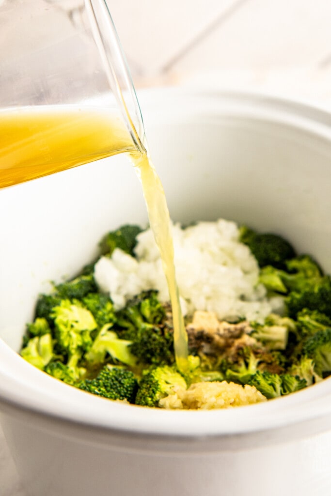 Pouring broth over soup ingredients in a slow cooker.