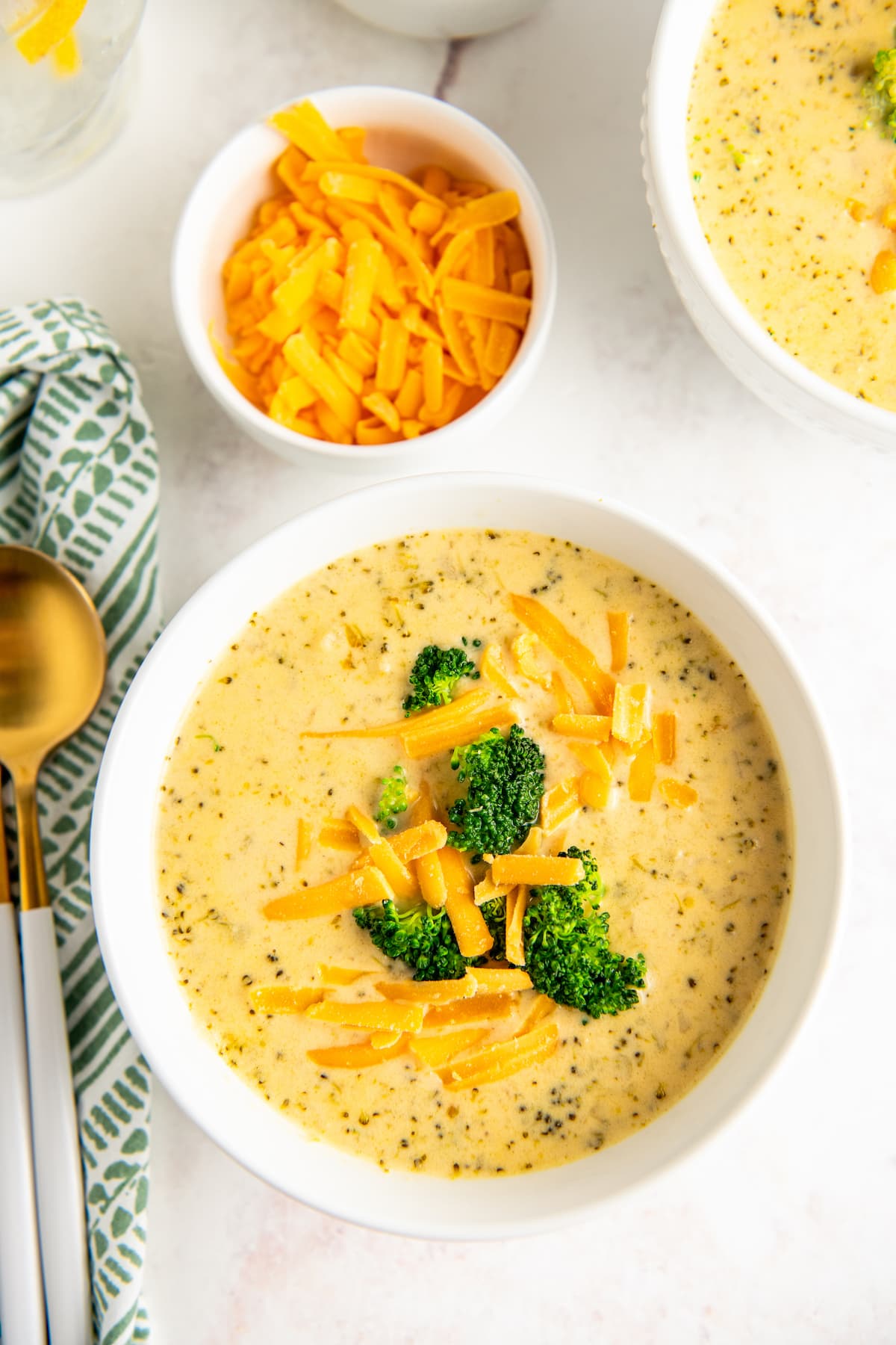 A bowl of soup, garnished with broccoli and cheddar.