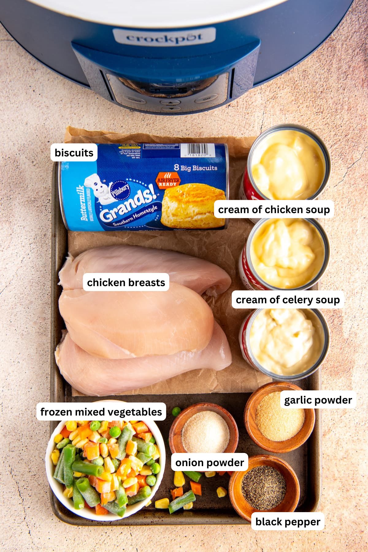 The ingredients for crockpot chicken pot pie recipe are in order from top to bottom: biscuits, chicken breasts, cream of chicken soup, cream of celery soup, frozen mixed vegetables, garlic powder, onion powder, black pepper.