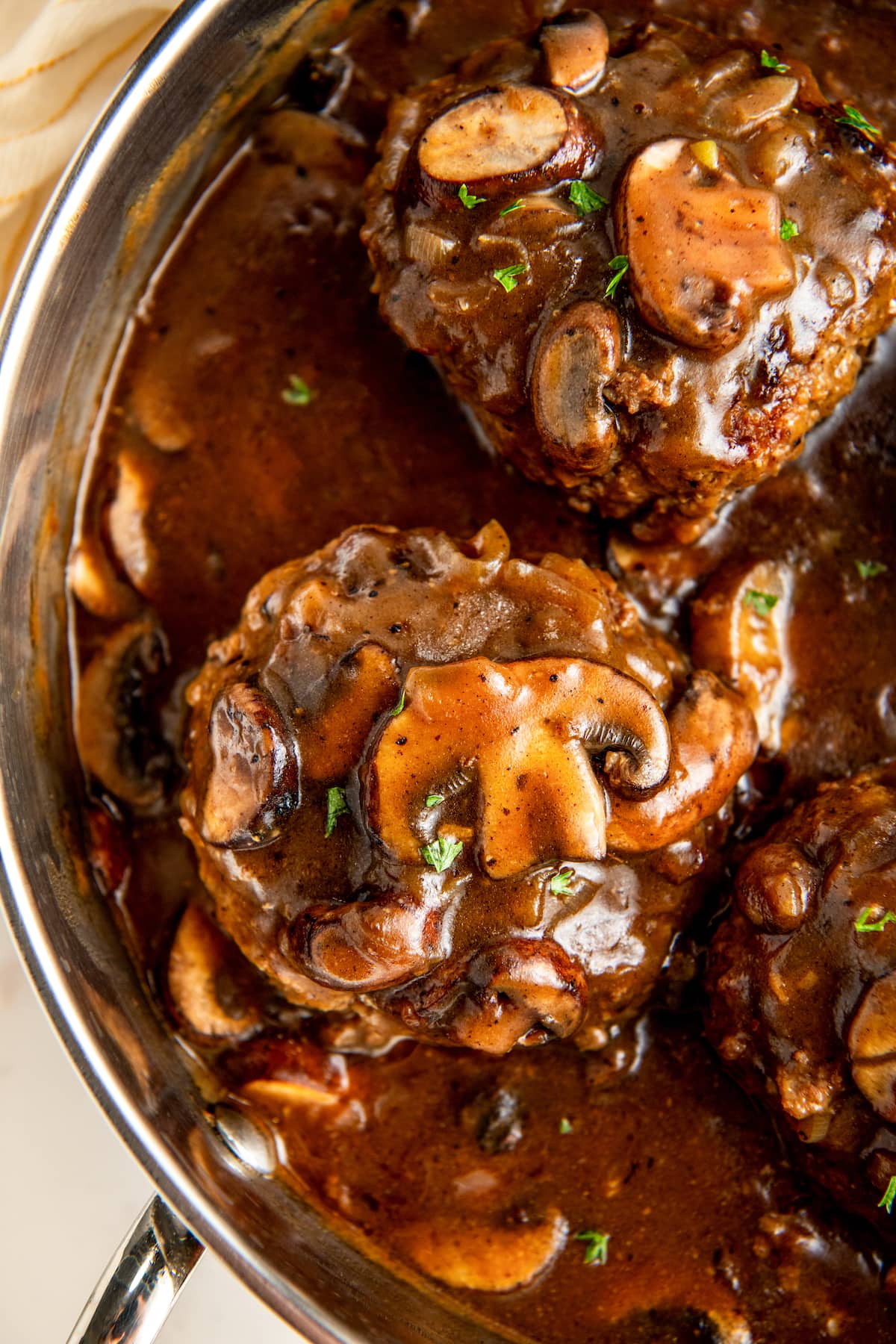 Salisbury steak in a skillet with brown mushroom and onion gravy.