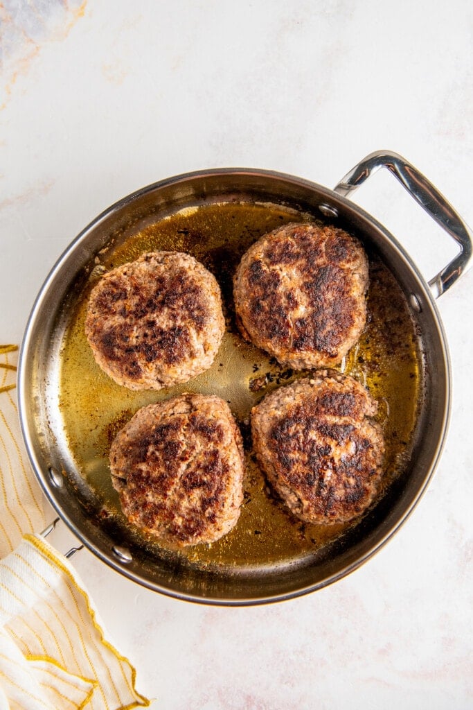 Hamburger patties cooking in a skillet.