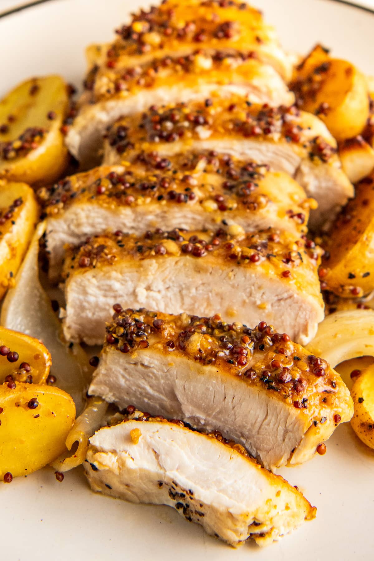 Honey mustard chicken sliced on a plate with potatoes.