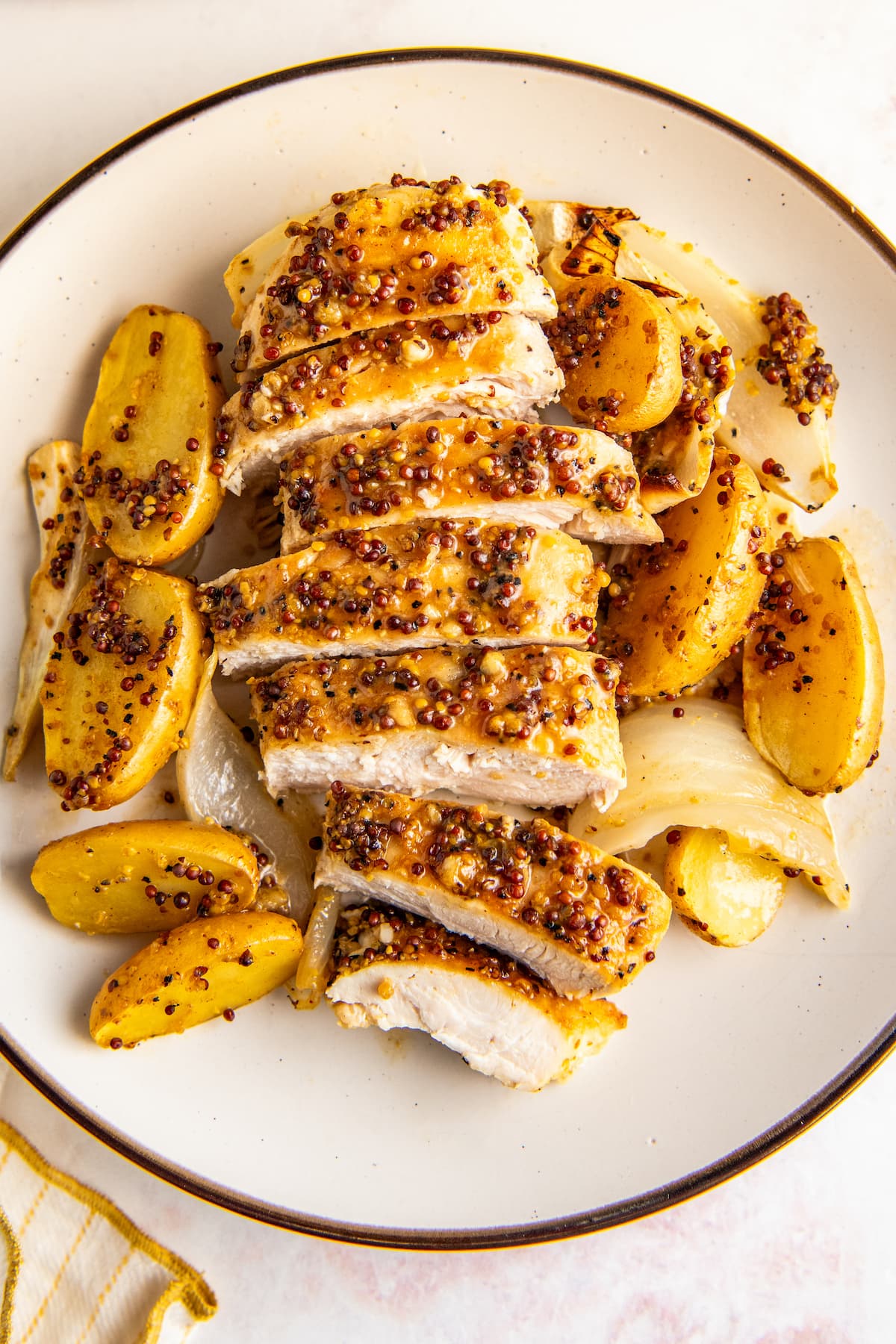 Slices of honey mustard chicken on a plate with potatoes and onions.