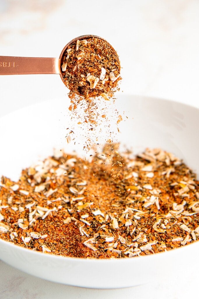 Homemade steak seasoning being poured into a bowl from a measuring spoon.