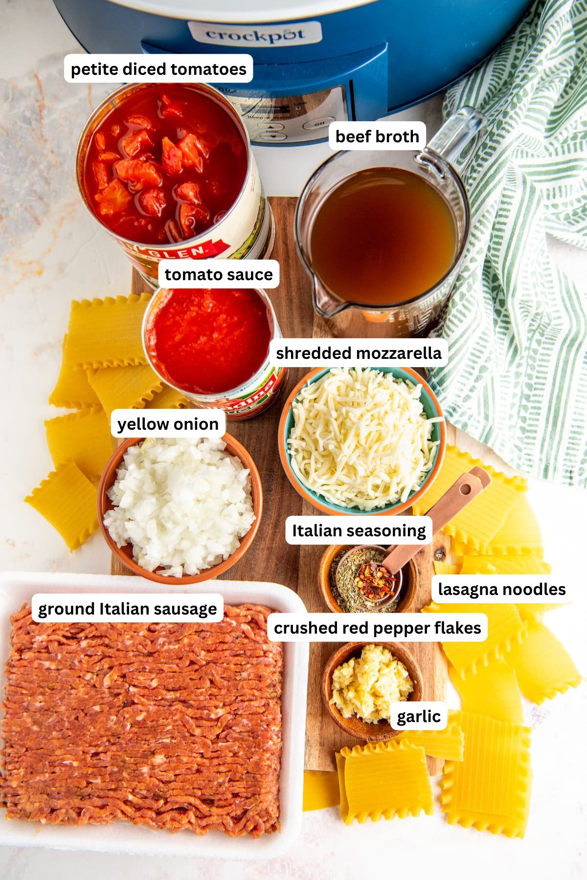 The ingredients for lasagna soup crockpot recipe in order from top to bottom: petite diced tomatoes, beef broth, tomato sauce, shredded mozzarella, yellow onion, ground italian sausage, crushed red pepper, italian seasoning, garlic, lasagna noodles.