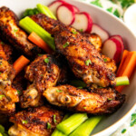 A bowl filled with cajun chicken wings, celery sticks, radishes, and carrots.