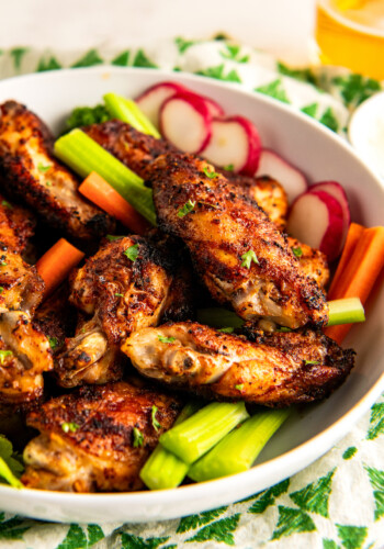 A bowl filled with cajun chicken wings, celery sticks, radishes, and carrots.
