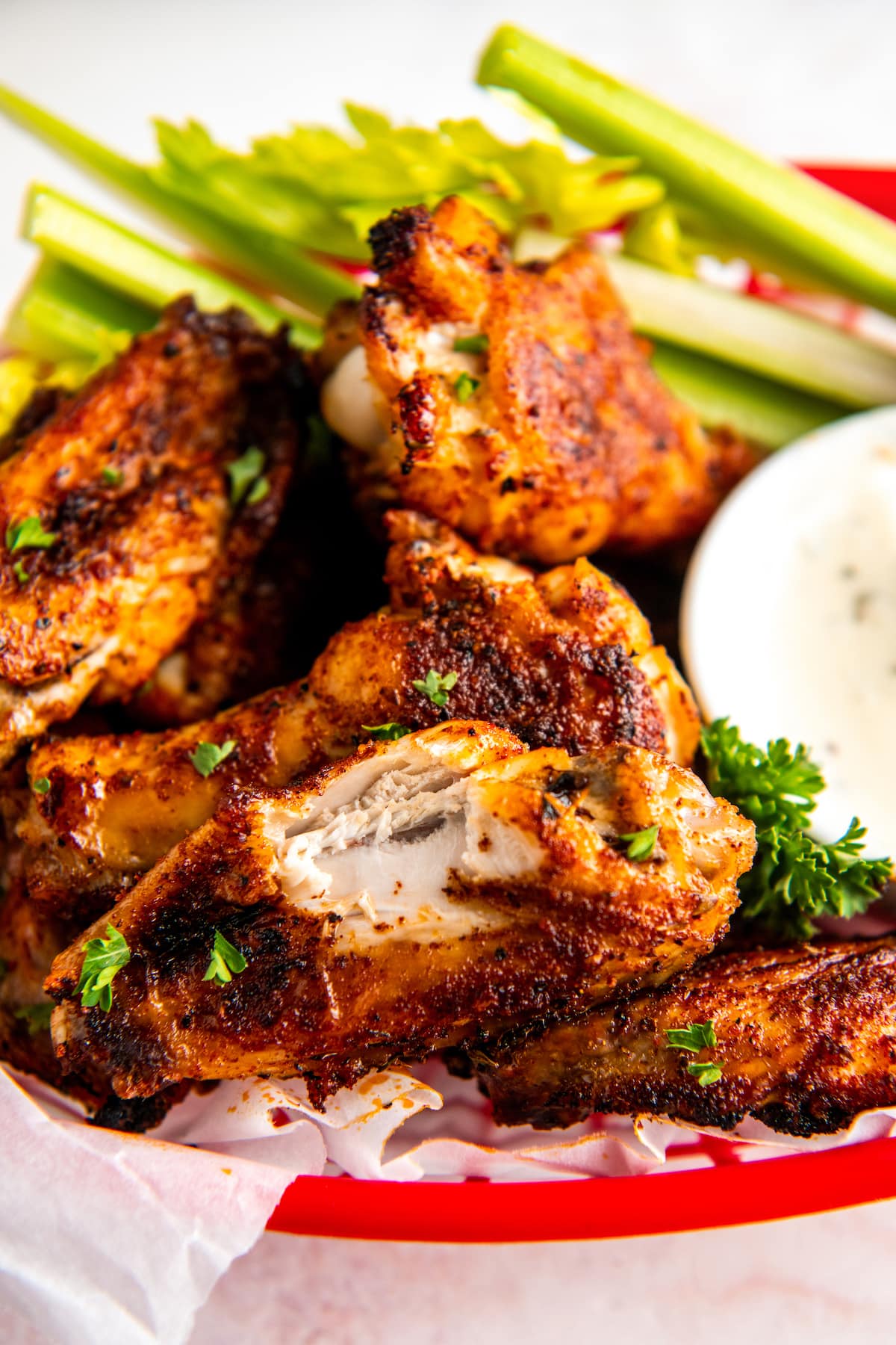 A plate with oven baked chicken wings, one which has a bite taken out of it, celery, and a bowl of ranch.