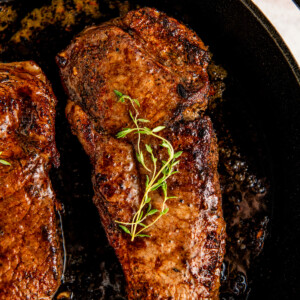 A juicy cast iron steak with a good sear topped with butter and herbs in a cast iron skillet.