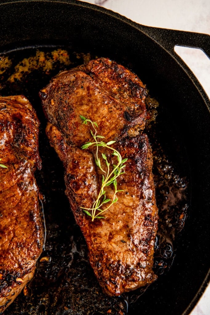 A juicy cast iron steak with a good sear topped with butter and herbs in a cast iron skillet.