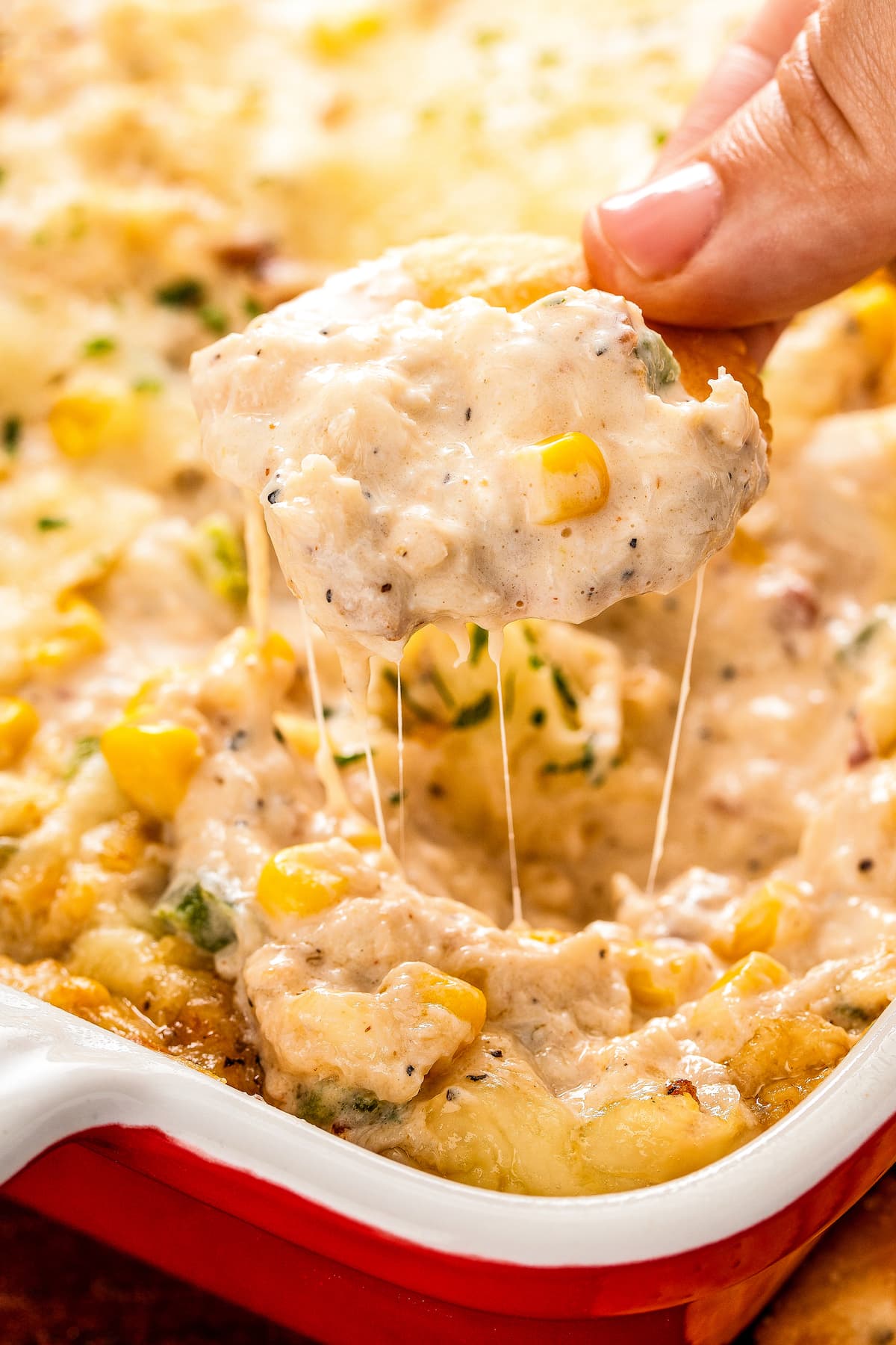 Fingers holding a Ritz cracker covered in Cajun crab dip, over a casserole dish full of dip.