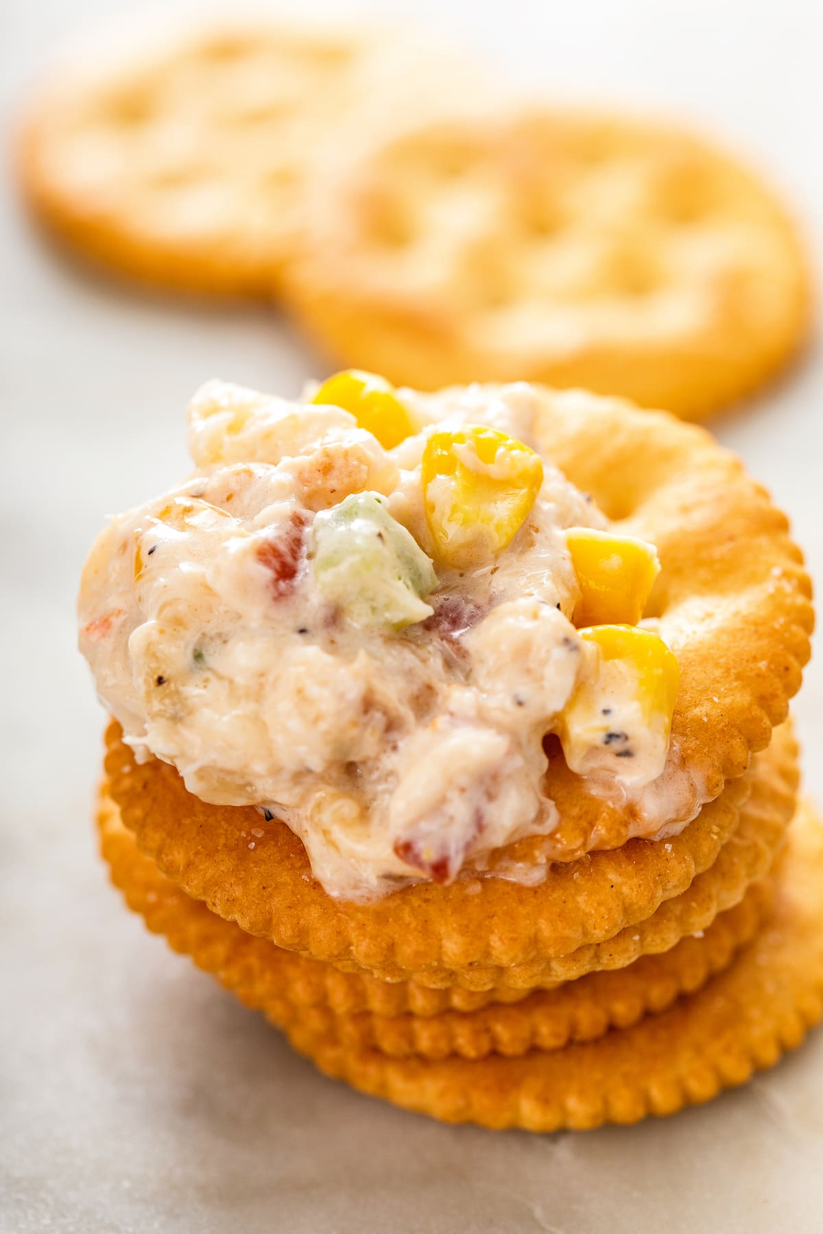 A stack of Ritz crackers with hot crab dip on top, with more crackers in the background.