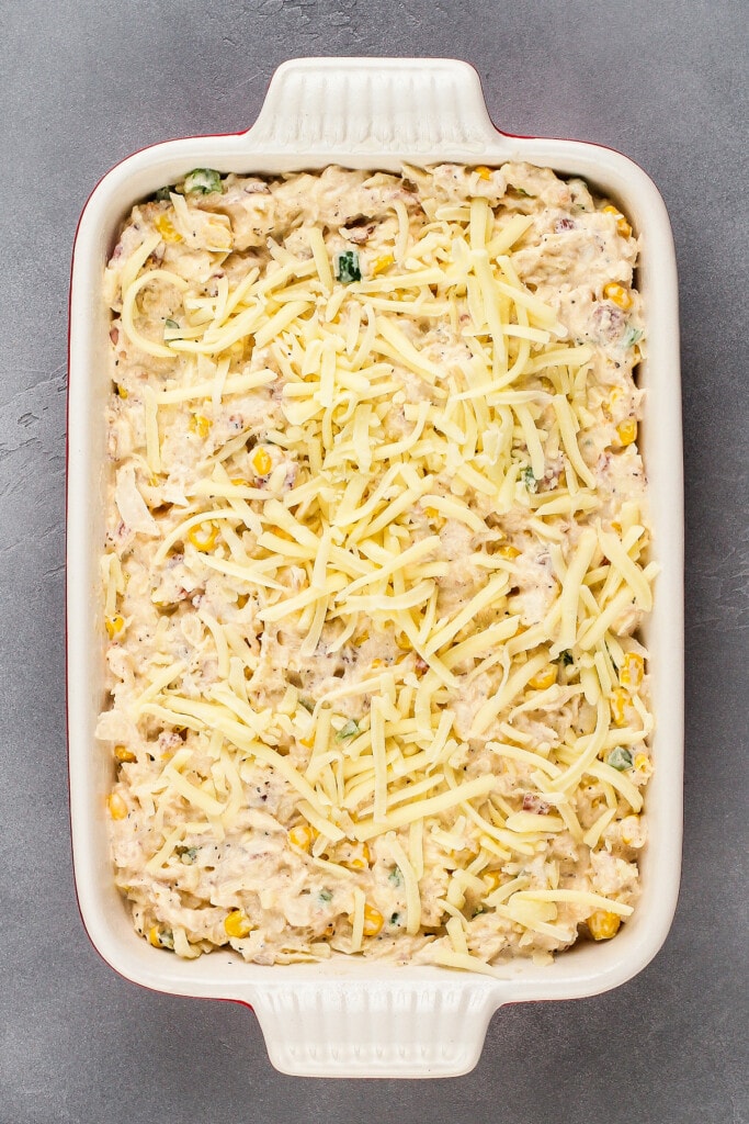 Overhead view of a casserole dish full of uncooked crab dip, topped with shredded cheese.