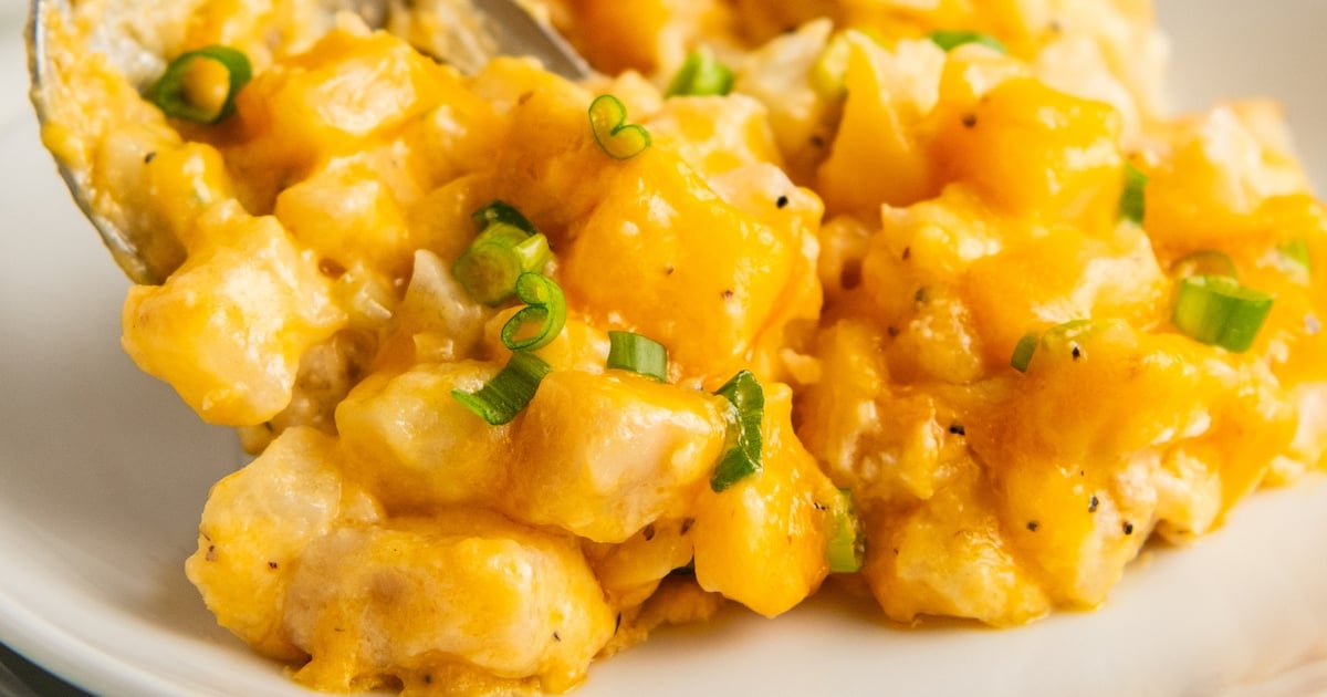 Close up of cheesy potatoes on a plate, topped with green onions.