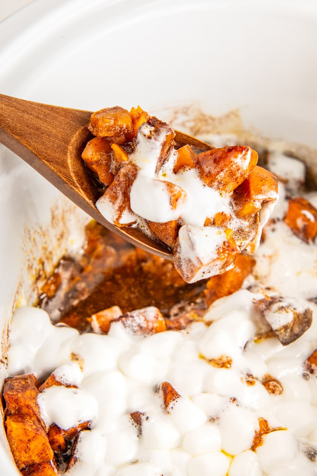 A wooden spoon removing a serving of sweet potato casserole from a crockpot.