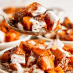 A spoon with sweet potato casserole covered in melted marshmallows, with plates of casserole in the background.