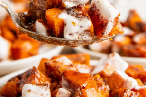 A spoon with sweet potato casserole covered in melted marshmallows, with plates of casserole in the background.