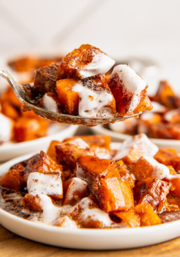 A spoon with sweet potato casserole covered in melted marshmallows, with plates of casserole in the background.