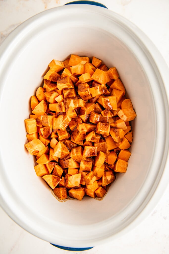 Overhead view of seasoned sweet potato cubes in a crockpot.