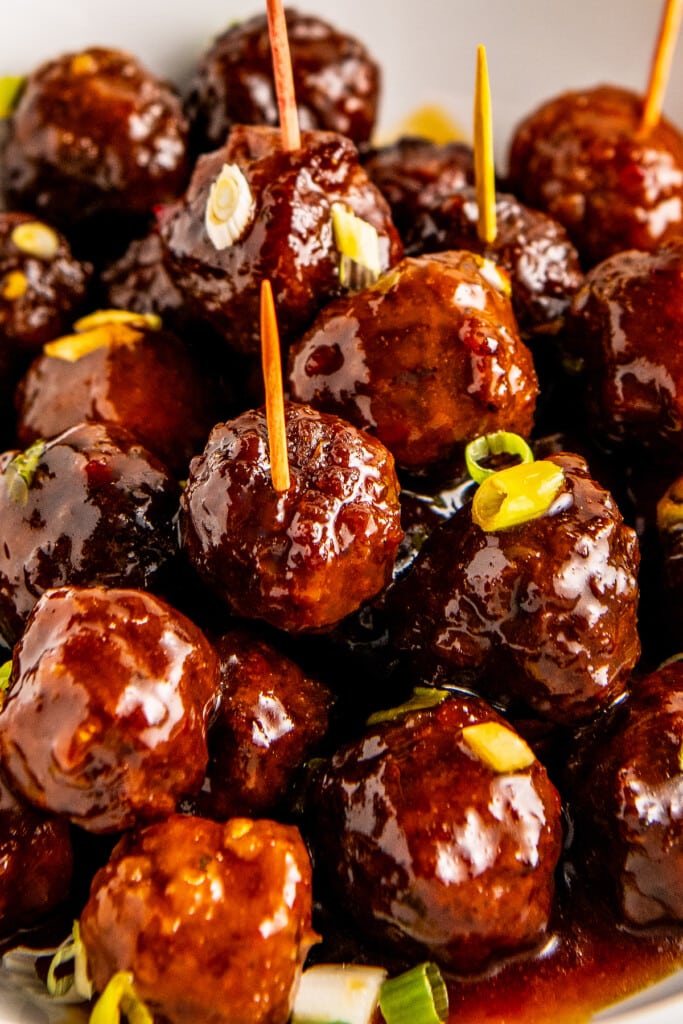 A plate of crockpot meatballs in a sweet and sour sauce with toothpicks interested in the top for easy serving.