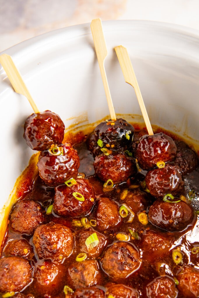 Sweet and sour meatballs in the crock-pot with small wooden skewers stuck through three meatballs to create an easy to grab appetizer.