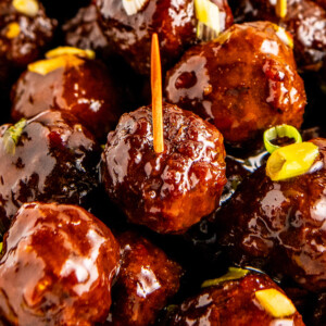 Close up of sweet and sour meatballs garnished with green onions, with a few toothpicks in them.