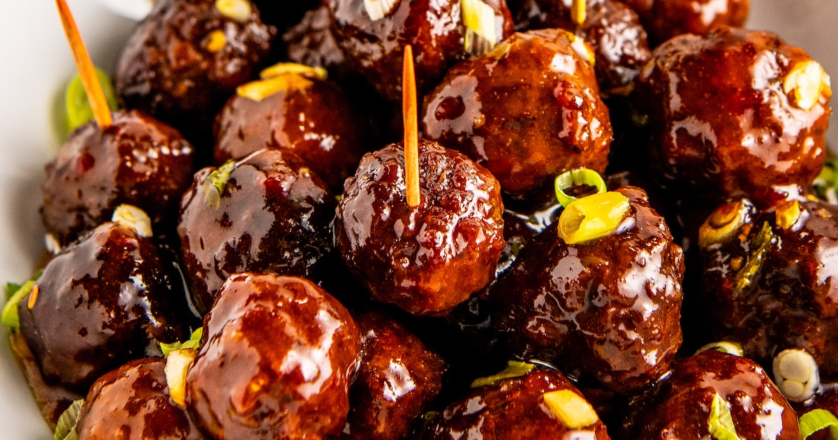 Close up of sweet and sour meatballs garnished with green onions, with a few toothpicks in them.